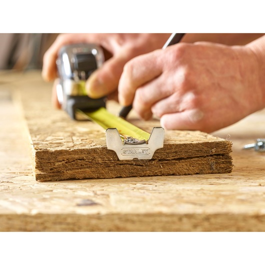 STANLEY 5-33-891 tape measure in use for marking wood, close-up of yellow blade and metal tip.