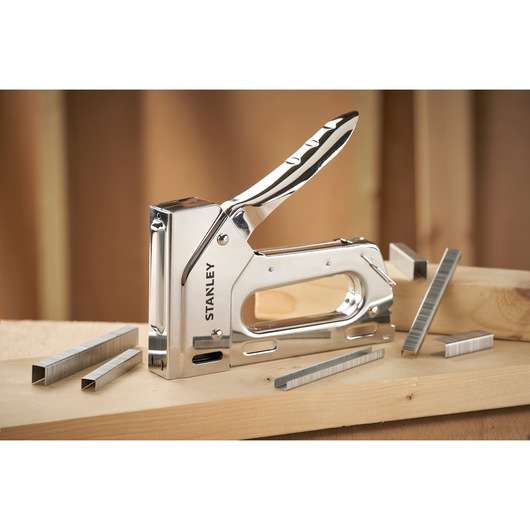 STANLEY 6-TR110 heavy-duty stapler with chrome finish and staples, angled on wooden planks.