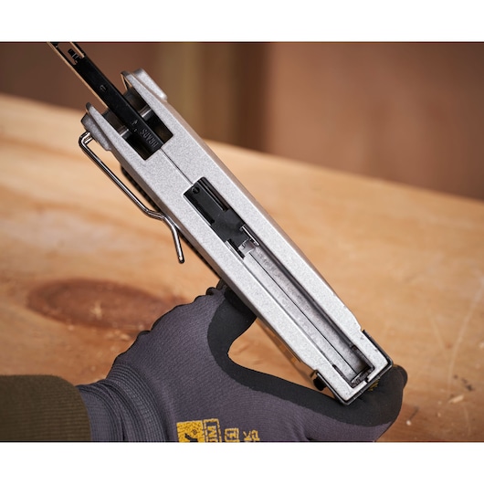 STANLEY 6-TR350 heavy-duty stapler, silver, angled view, held by a gloved hand over a wooden surface.