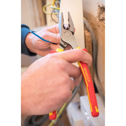 STANLEY 84-002-S pliers with red and yellow handles gripping a blue wire during electrical work.