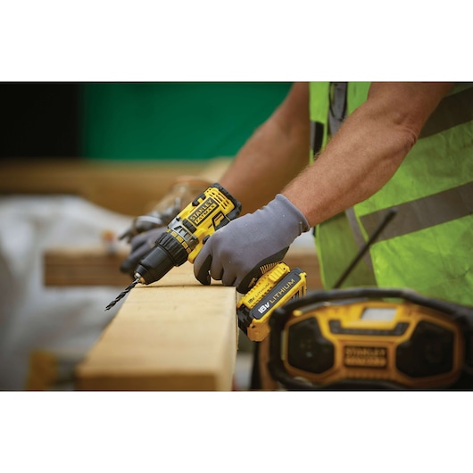 STANLEY FMC600B cordless drill in use, yellow and black, worker with gloves drilling wood, outdoor setting.