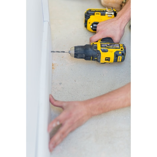 STANLEY FMC607B cordless drill in use, yellow and black, drilling into white material, close-up view.
