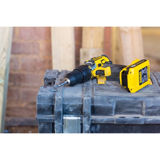 STANLEY FMC625D2 cordless drill with yellow and black design, lying on a dusty toolbox, side view.