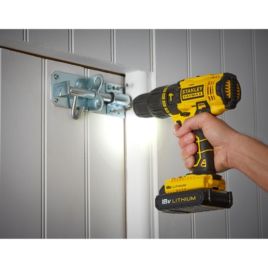 STANLEY FMC626C2K cordless drill, yellow and black, screwing latch on white door, side angle.