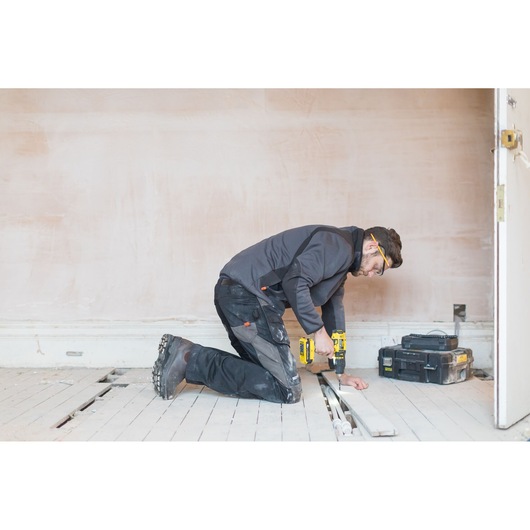 STANLEY FMC626C2K worker kneeling, using cordless drill, toolbox in background, indoor construction site.