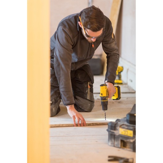 STANLEY FMC626D2K cordless drill used on wood in construction setting, worker kneeling while drilling.