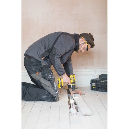 STANLEY FMC626D2K cordless drill used by worker kneeling on floor near tool case, side view, indoor photography.