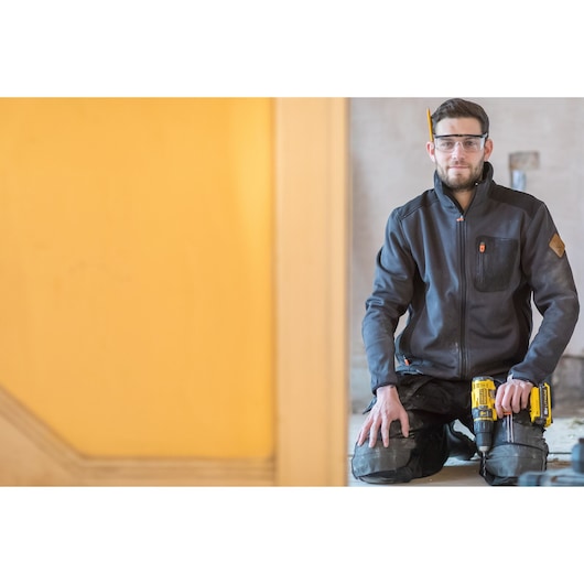 STANLEY FMC626D2K cordless drill held by worker in black jacket, indoor construction setting.