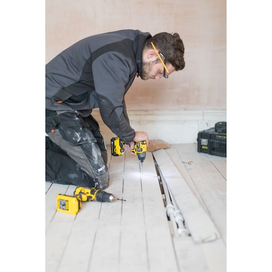 STANLEY FMC647B cordless drill used by worker on wooden floor, additional drill and tool case nearby.