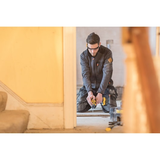 STANLEY FMC647B cordless drill in use on wood floor, man kneeling with tool case nearby, indoor setting.