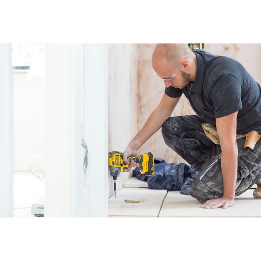 STANLEY FMC647B cordless drill used by worker for floor screw installation, indoor setting.