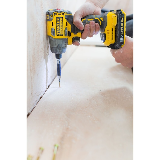 STANLEY FMC647D2 cordless impact driver held in hand driving screw into wood, side view.