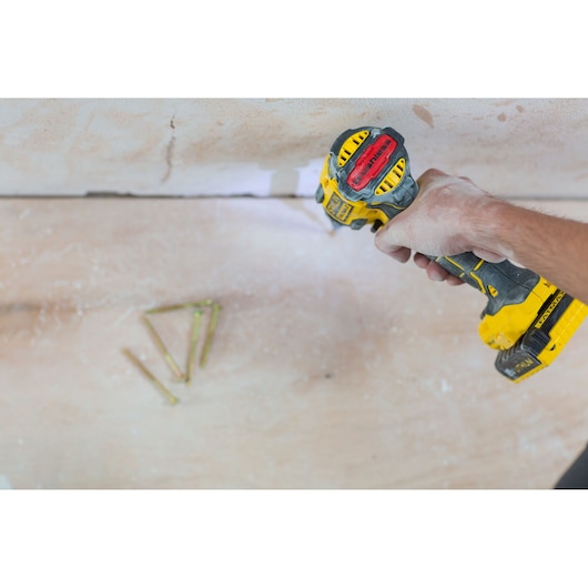 STANLEY FMC647D2 cordless drill in hand, side angle, used on a wall, yellow and black design, with visible screws.