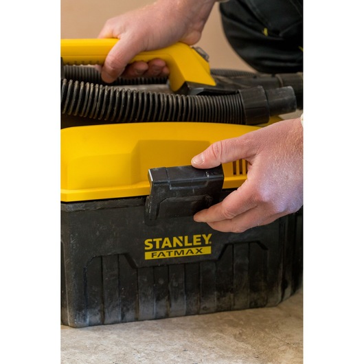 Photo of STANLEY FATMAX FMC795B portable wet dry vacuum with yellow handle and hose, close-up of hands using latch.