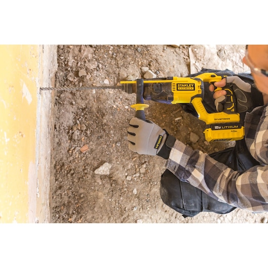 Photo of STANLEY FMCD900B rotary hammer drill in use, cordless, yellow and black, drilling into concrete wall.
