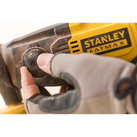 Close-up of gloved hand adjusting control knob on STANLEY FMCD900B power tool, showing yellow and black body.