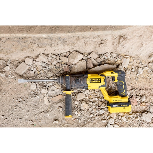 STANLEY FMCD900B rotary hammer drill, yellow and black, photographed on rocky construction ground.