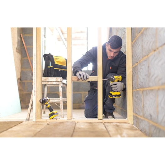 STANLEY FMCK461C2 drill driver in use at construction site, worker assembling wooden frame, tool bag and ladder nearby.
