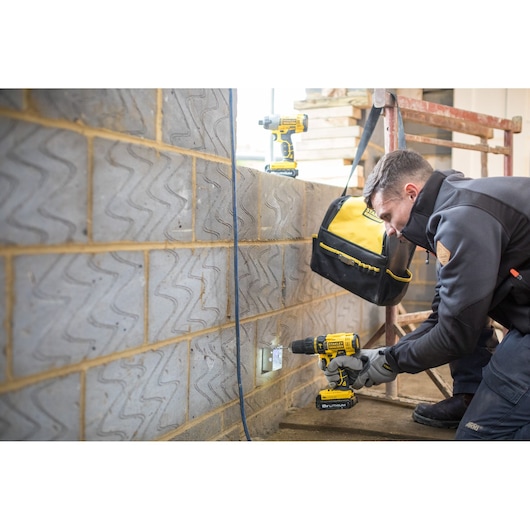STANLEY FMCK465C2S cordless drill in use by worker on brick wall, with tool bag and second drill visible.