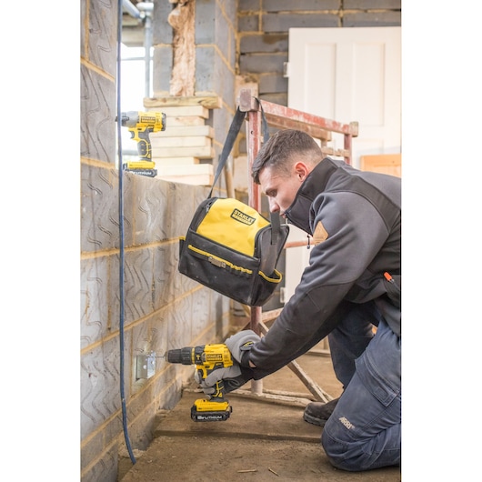 STANLEY FMCK465C2S drill and bag in use on construction site, worker kneeling near brick wall.