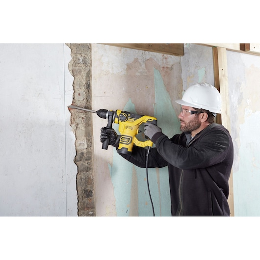 STANLEY FME1250K rotary hammer drill in use on wall, yellow and black power tool held by worker with hard hat.