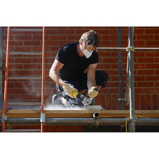 STANLEY FME821 angle grinder in use by worker cutting material outdoors with protective gloves and mask.