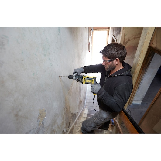Stanley FMEH1100K corded drill in use drilling into wall, product photography, side angle.