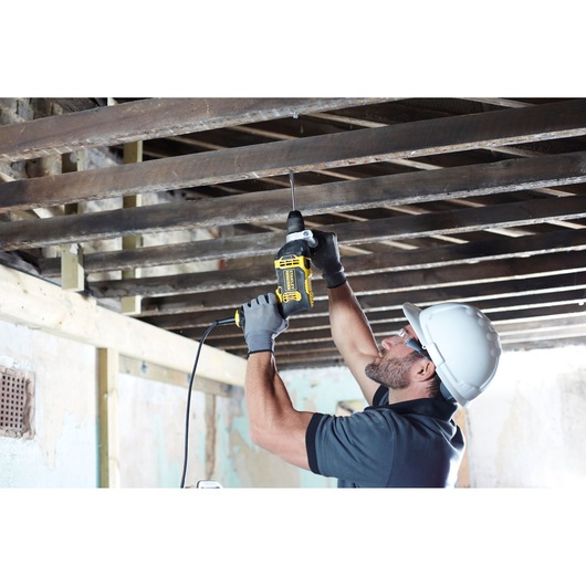 STANLEY FMEH750K corded drill used overhead on wooden beams, side angle, construction setting.