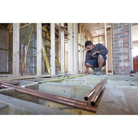 STANLEY FMHT0-36326 tape measure photography in use measuring floorboards at construction site.