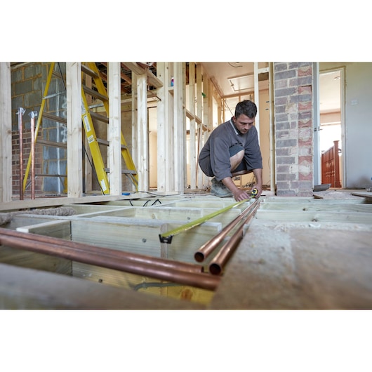 STANLEY FMHT0-36326 tape measure used by worker measuring copper pipes in a house renovation scene.