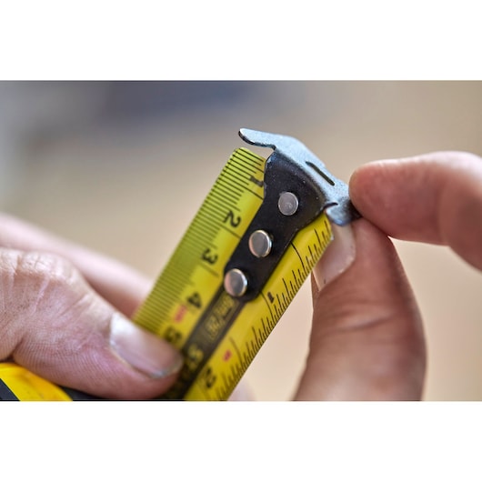 Close-up photo of STANLEY FMHT0-36326 tape measure blade with yellow markings held between fingers.