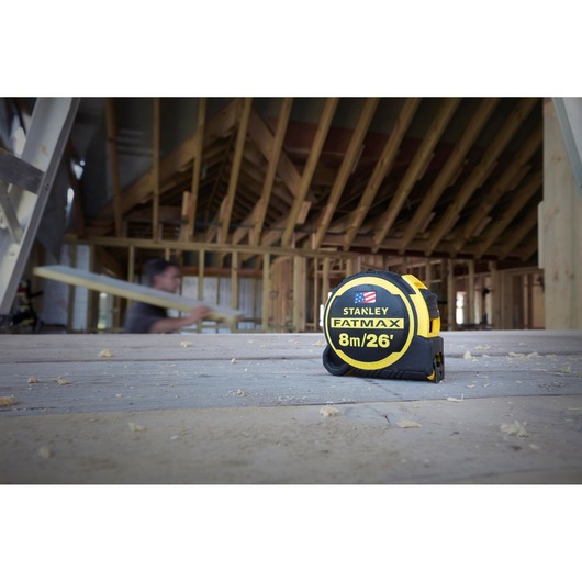 STANLEY FATMAX 8m/26' tape measure FMHT0-36326 on a construction site floor, wood framing in background.