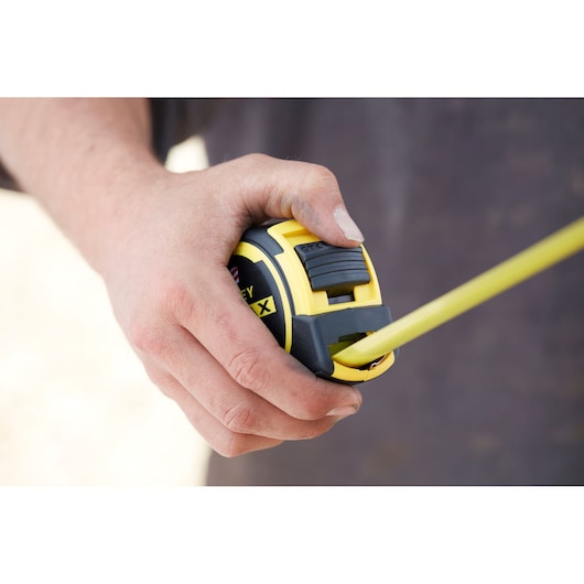 STANLEY FMHT0-36326 tape measure held in hand, yellow and black, photography close-up.