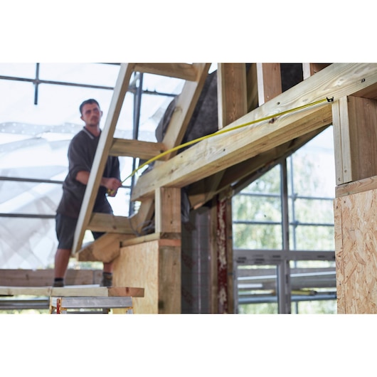 STANLEY FMHT0-36327 tape measure used for measuring wood beams at a construction site.