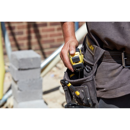 Photo of STANLEY FMHT0-36327 tape measure in tool belt pocket at a construction site.