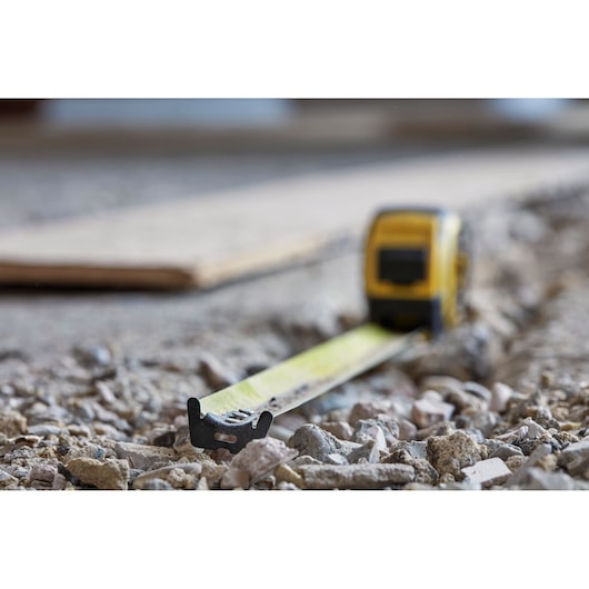 STANLEY FMHT0-36327 tape measure extended on rocky ground, close-up photography.