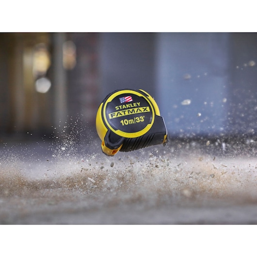 STANLEY FMHT0-36336 FATMAX tape measure 10m/33', yellow and black, shown impacting debris on ground.