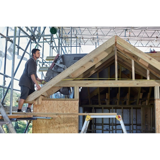 STANLEY FMHT0-36336 tape measure used by worker on wooden roof construction site.