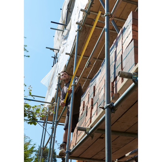 STANLEY FMHT0-36336 tape measure held by construction worker on scaffolding at building site.