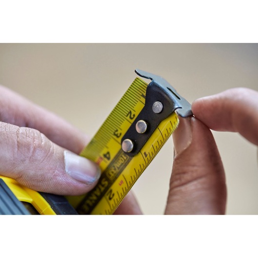 STANLEY FMHT0-36336 tape measure close-up showing yellow blade and metal hook held by hands.