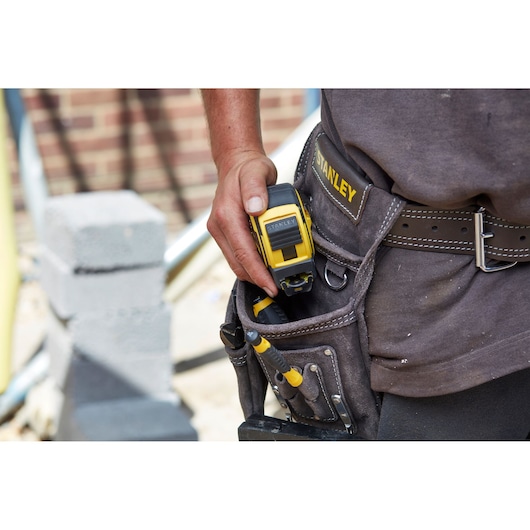 STANLEY FMHT0-36337 tape measure in a tool belt pocket with screwdrivers on a construction site.