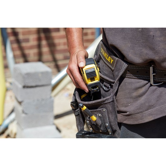 Stanley FMHT0-36337 tape measure in tool belt pocket, photography close-up on construction site.