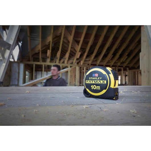 Photo of STANLEY FMHT0-36337 FATMAX 10m tape measure on wooden floor at construction site.