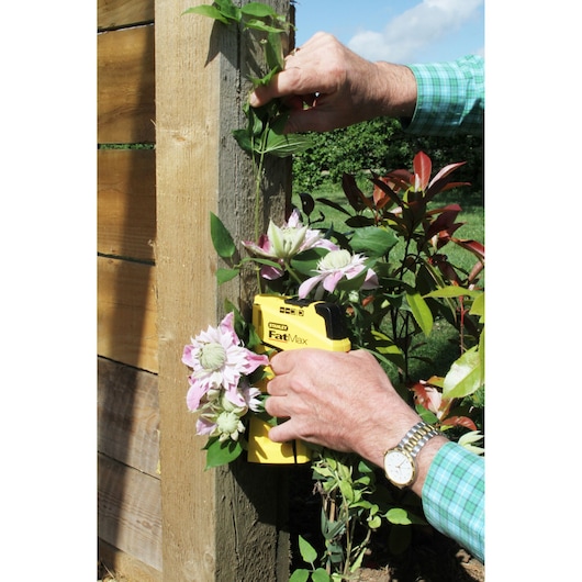 STANLEY FMHT0-70411 stapler securing vine to wooden post among blooming flowers outdoors.