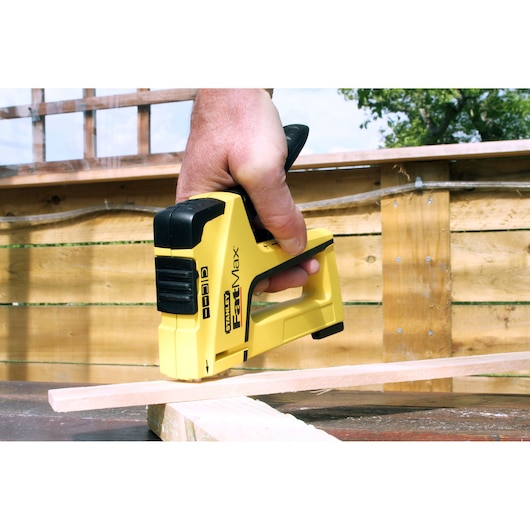 Photo of STANLEY FMHT0-70411 stapler in use on wood, yellow and black, outdoor setting.