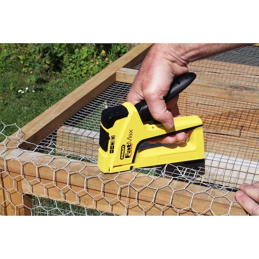 STANLEY FMHT0-70411 staple gun in use fastening wire mesh to wooden frame outdoors.