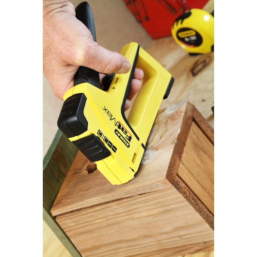 Photo of STANLEY FMHT0-70411 yellow hand stapler in use on wooden surface, close-up angle.