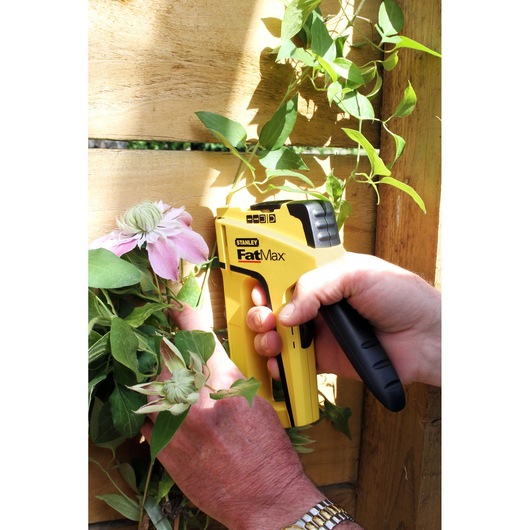 STANLEY FatMax FMHT0-70411 stapler held by hand attaching plant to wooden fence.