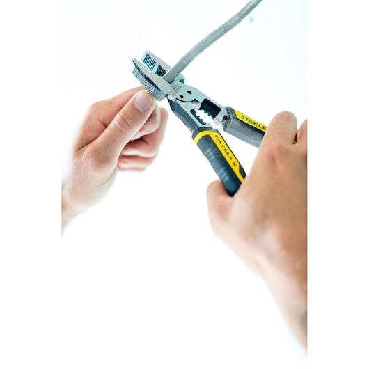 STANLEY FMHT0-75469 pliers with black and yellow handles cutting cable, close-up with hands, product photography.