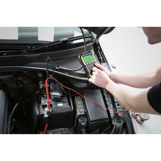 Photo of STANLEY FMHT0-77419 automotive multimeter testing a car battery, top view of engine compartment.
